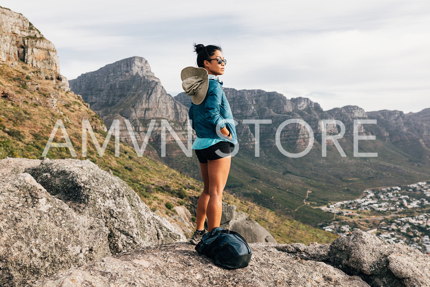 Young woman in sport clothes with backpack looking at the view while standing on a cliff