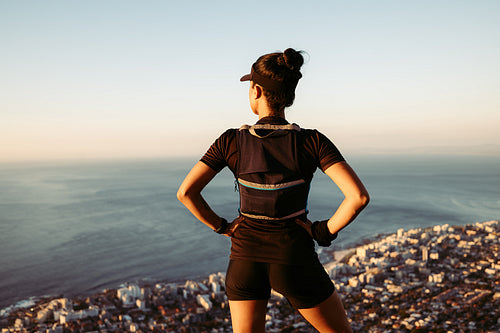 Rear view of sportswoman looking at the view from top. Female with her hands on hips enjoying a view.