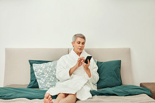 Senior woman typing on her smartphone lying on a bed