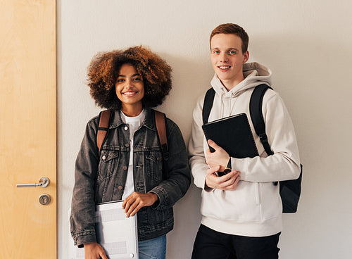 Two smiling classmates standing together at wall and looking at camera