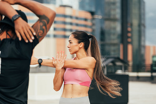 Young slim woman stretching her arm on a rooftop