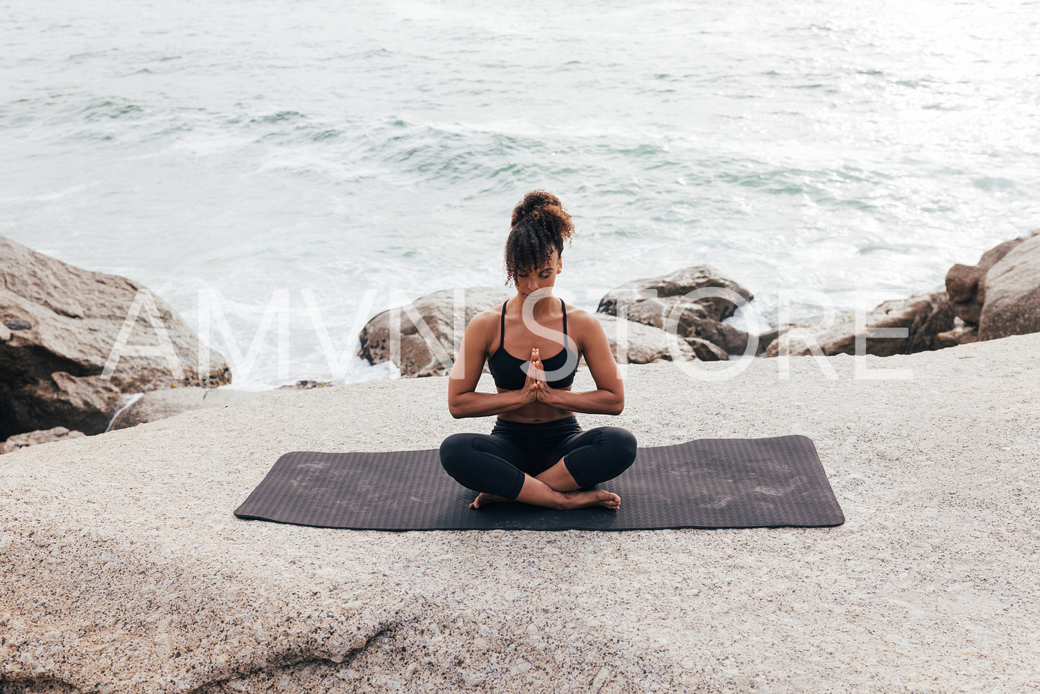 Woman in praying pose sitting on mat with closed eyes by ocean