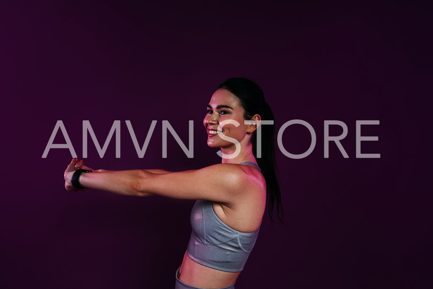 Young smiling woman stretching and flexing her hands over magenta background in studio