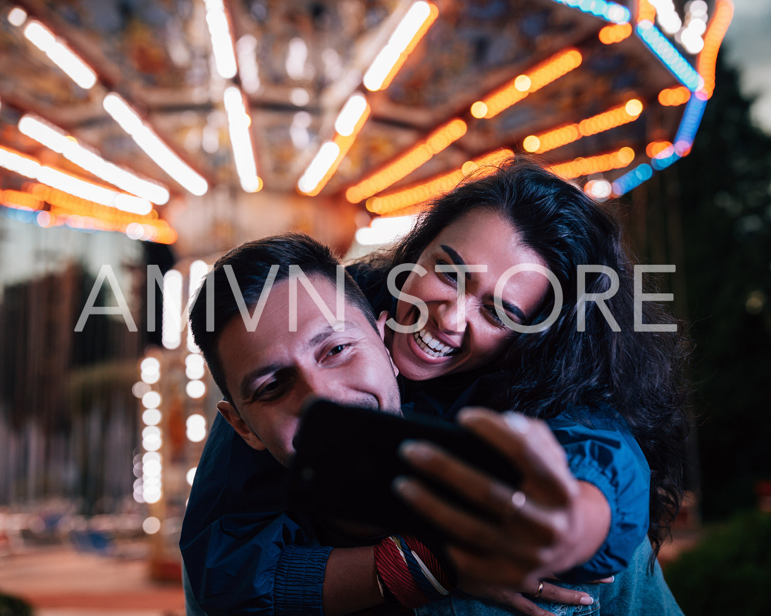 Young happy couple taking selfie while having fun at night in an amusement park