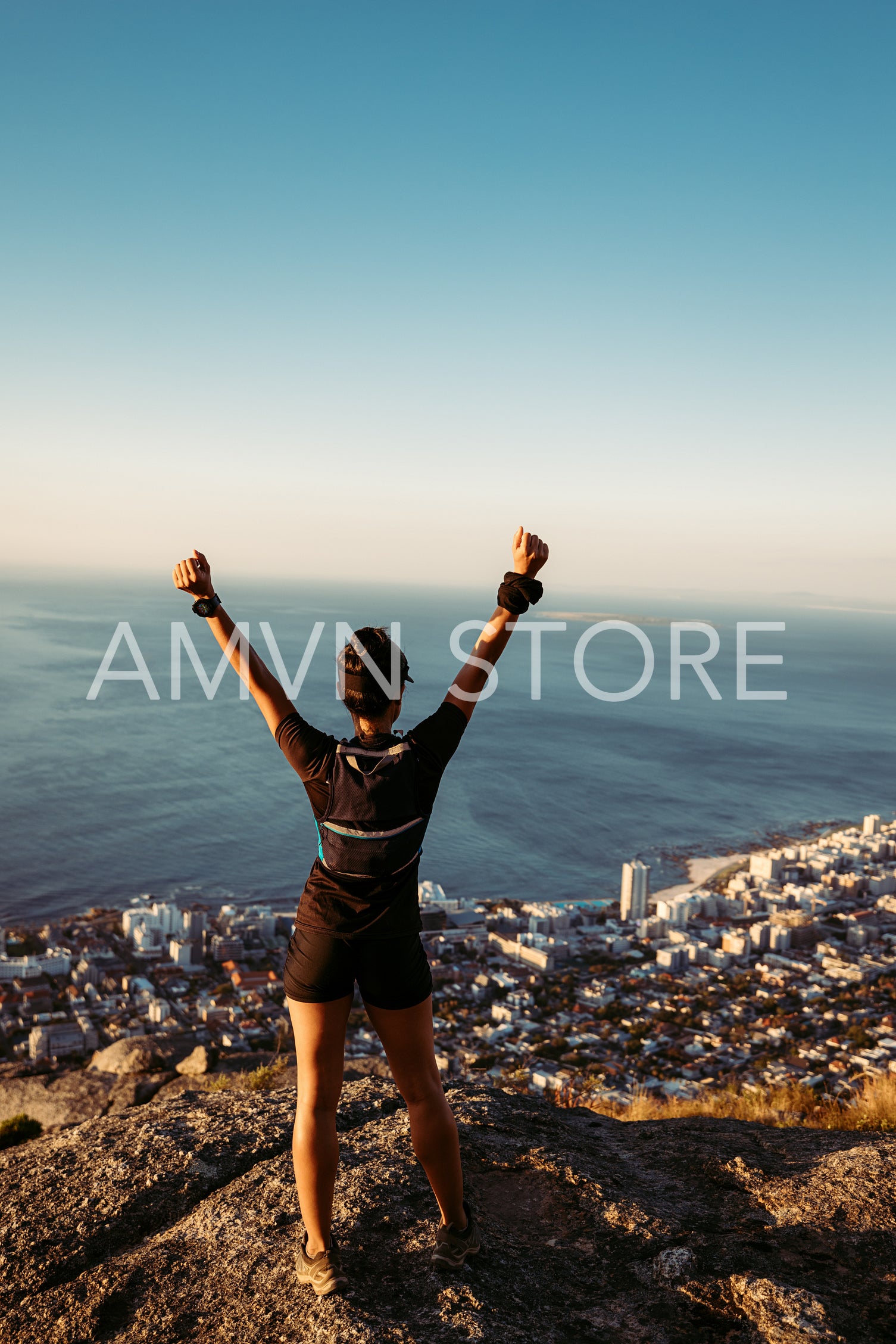 Rear view of young woman standing on mountain top looking at view with arms wide open. Young female enjoying the view from the top at sunset.