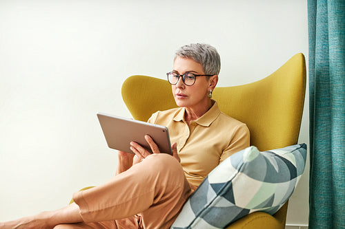 Stylish senior woman holding a digital tablet while sitting in living room