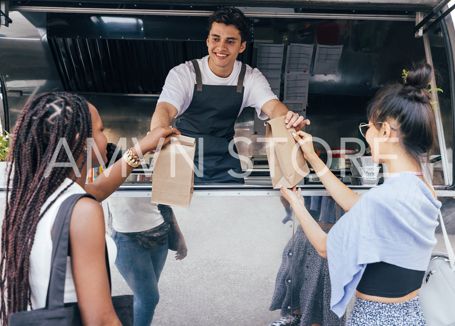 Two female friends receiving packaged food from a young business owner at a food truck