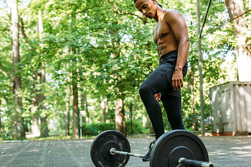 Side view of a young bare-chest athlete adjusting barbell for training