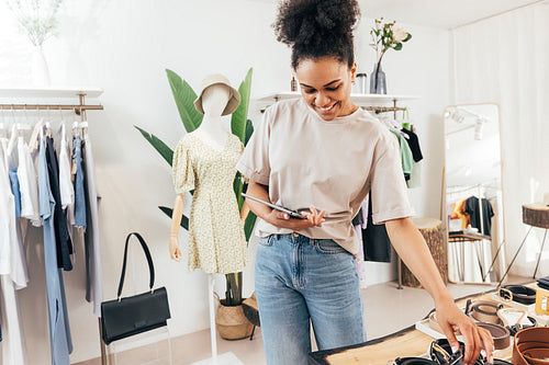 Young saleswoman using a digital tablet at store. Business owner working with merchandise in her retail shop.