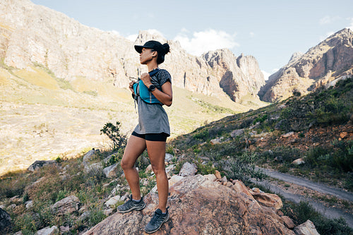 Side view of trail runner in sports wear standing in valley. Young female in fitness attire in wild terrain.