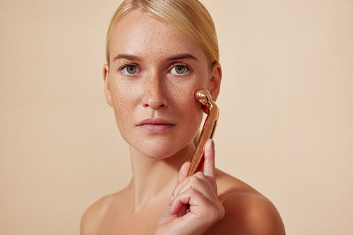 Young woman with smooth skin using a facial roller. Blond female doing skincare routine.