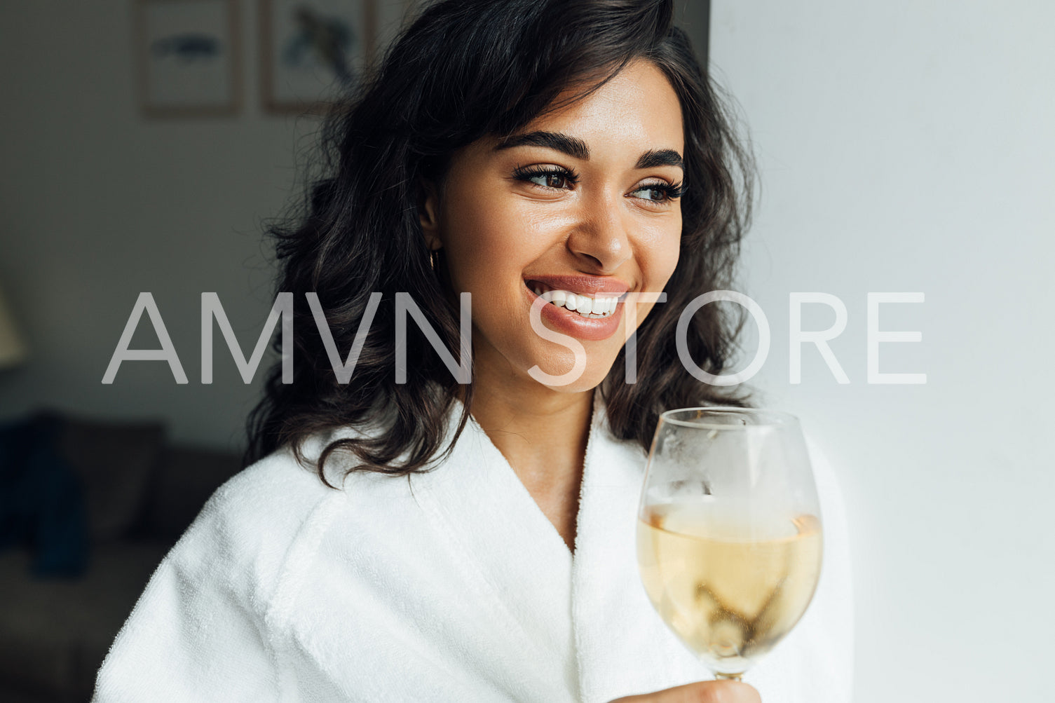 Beautiful cheerful woman with bocal of wine standing in living room. Young female relaxing at home alone.	