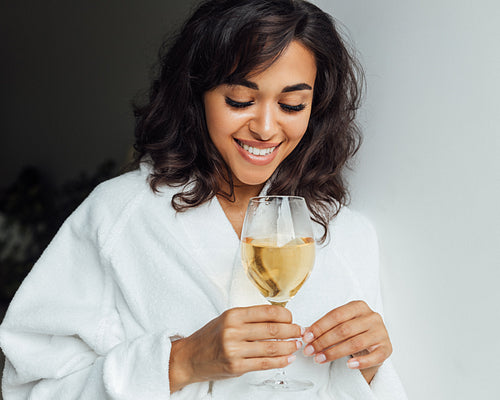 Beautiful woman relaxing at home. Smiling female looking at bocal with wine.