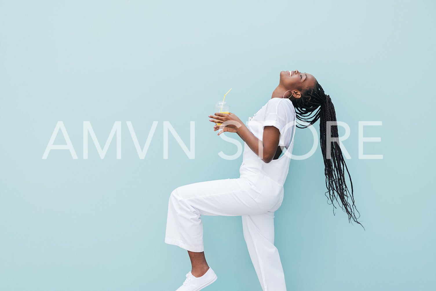 Side view of woman in white clothes having fun against blue wall. Young female holding a juice enjoying good mood.