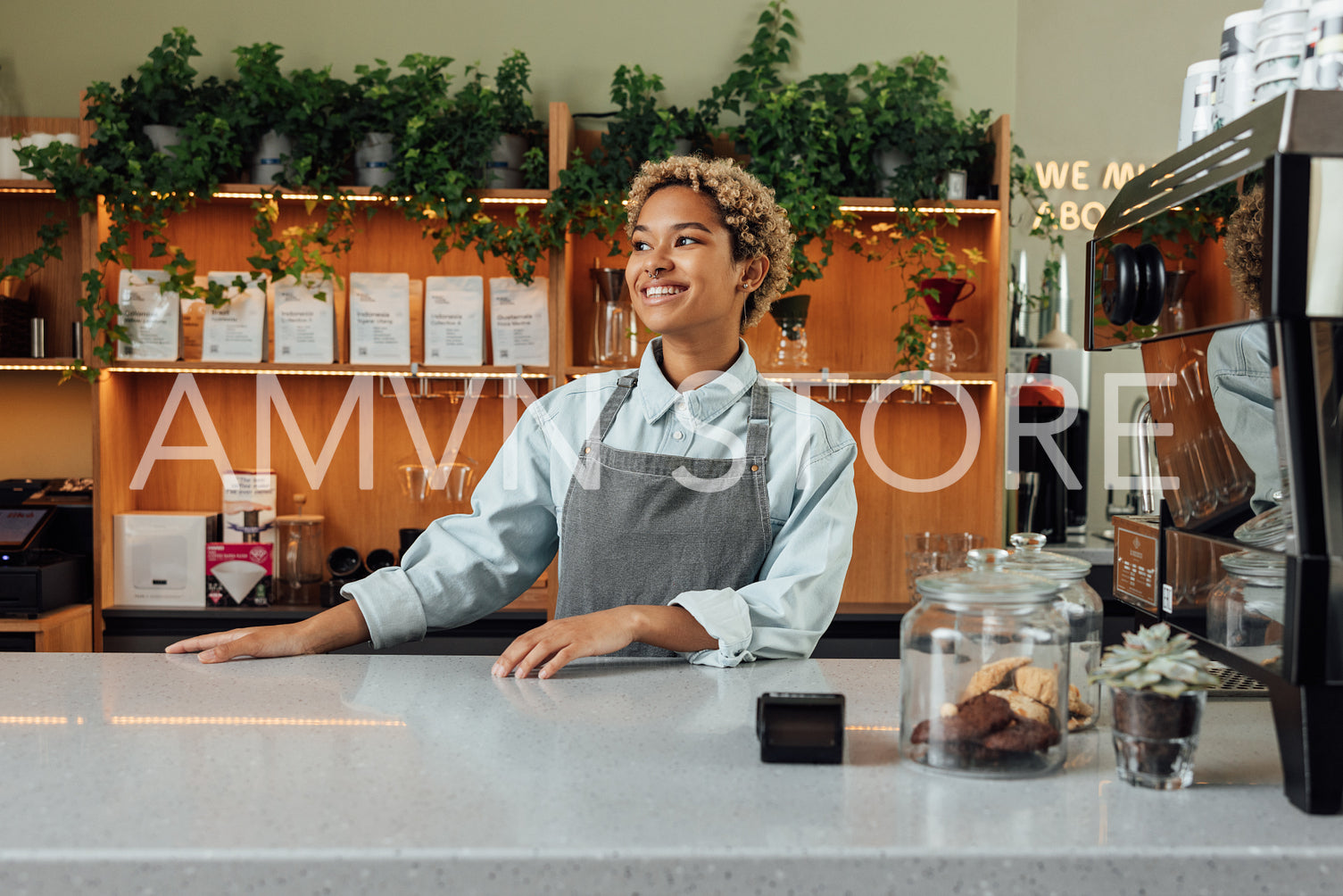 Smiling female bartender looking away while standing at the counter. Young barista in an apron.