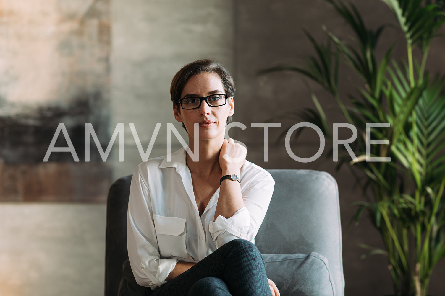 Confident businesswoman in eyeglasses sitting on a grey armchair in her loft