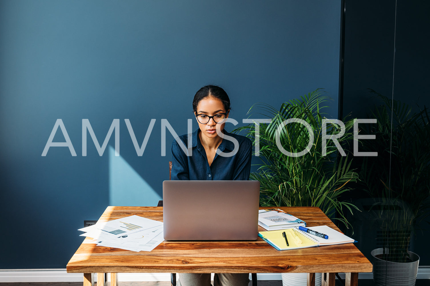 Serious woman sitting at a table and working remotely on a laptop from home	