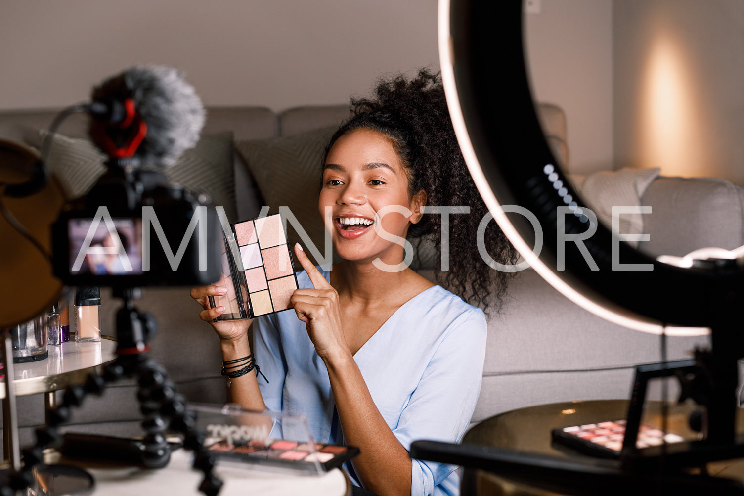 Laughing female holding an eyeshadow palette while filming a video for her beauty vlog