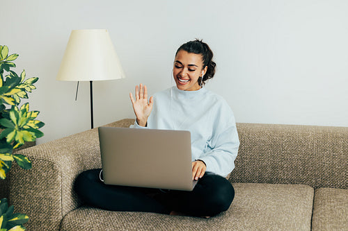 Smiling woman sitting on sofa in living room making gestures on a video call