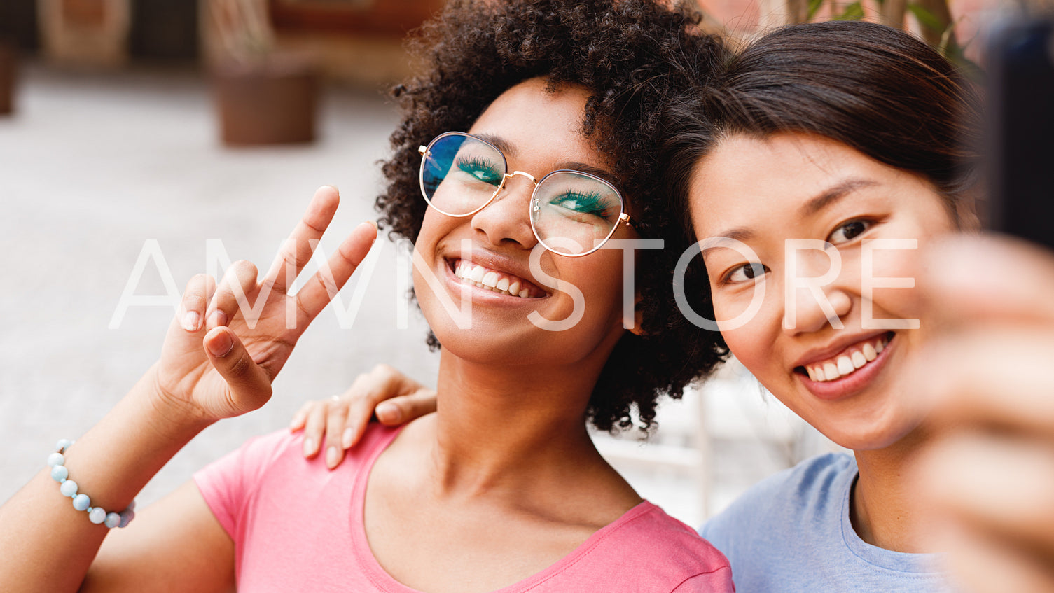 Two happy friends looking at smartphone and taking selfie, sitting in outdoor cafe	