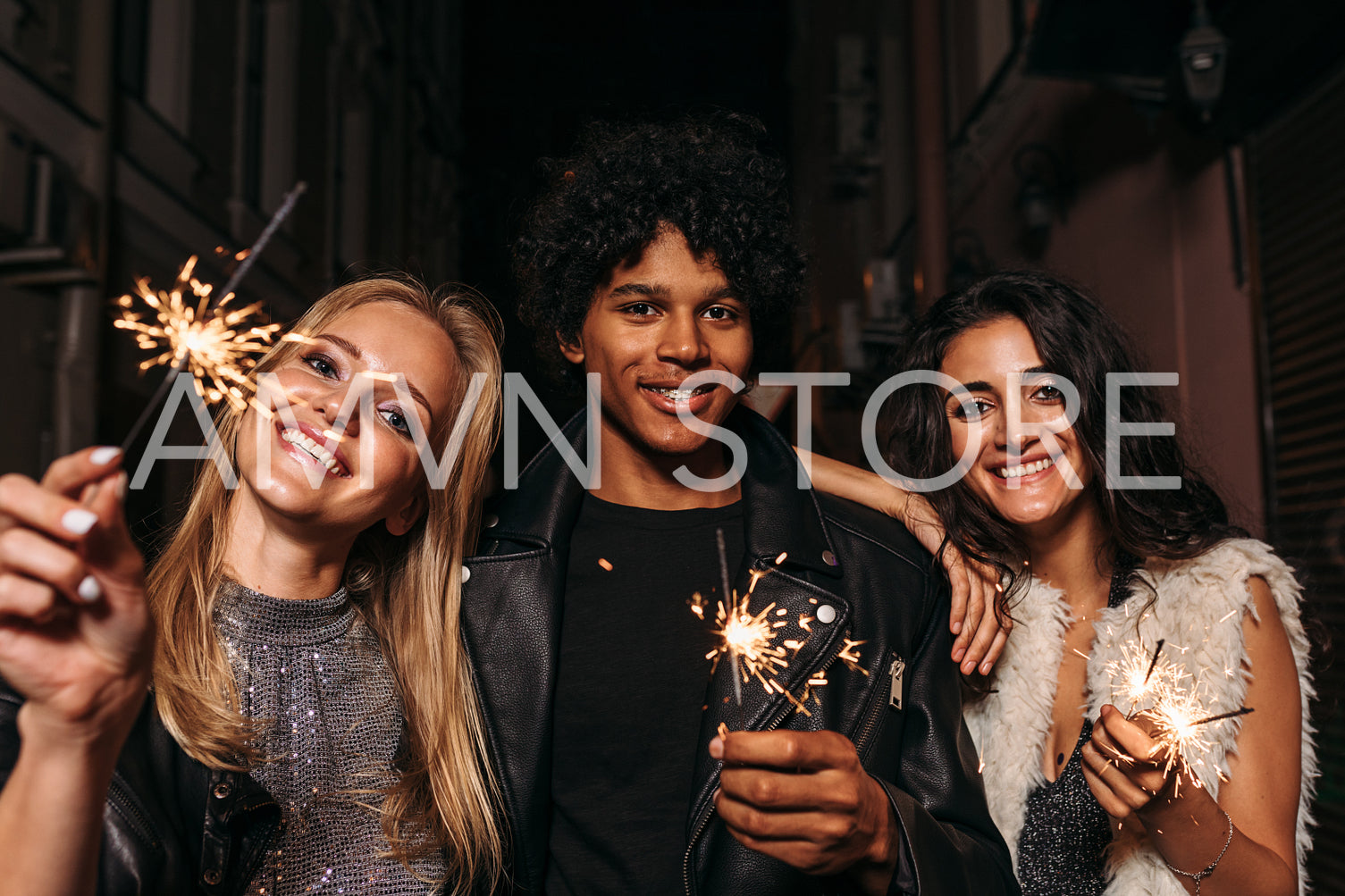 Group of friends standing on sidewalk at night, holding sparklers	