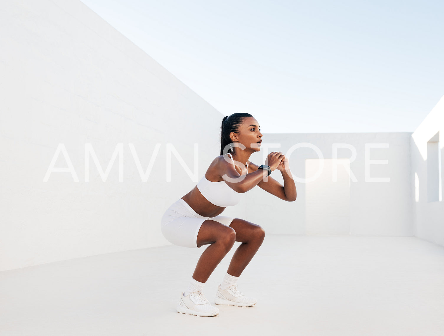 Female fitness influencer doing sit-ups in a white outdoor studio. Young woman doing workout outdoors. Female in white fitness attire is doing exercises for her glutes.