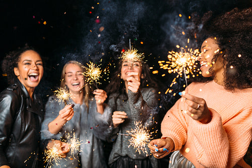 Four happy women holding sparklers, throwing confetti