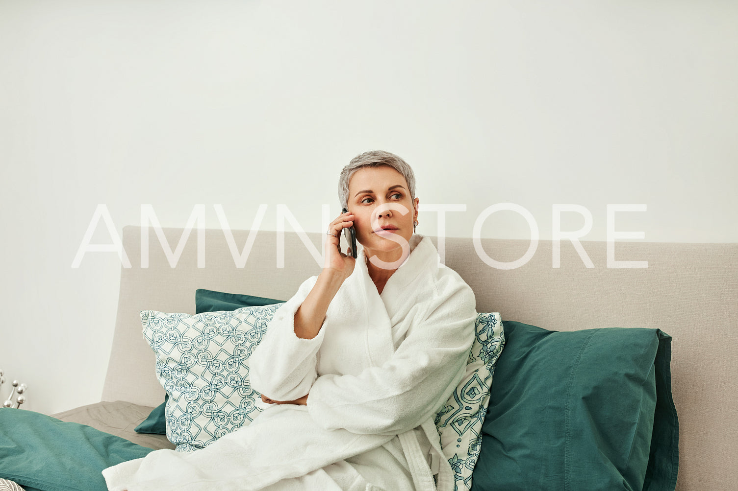 Mature woman wearing bathrobe making phone call from bedroom