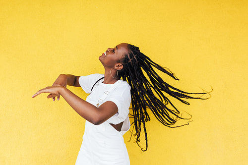 Side view of young happy woman with long braids dancing at yellow wall outdoors