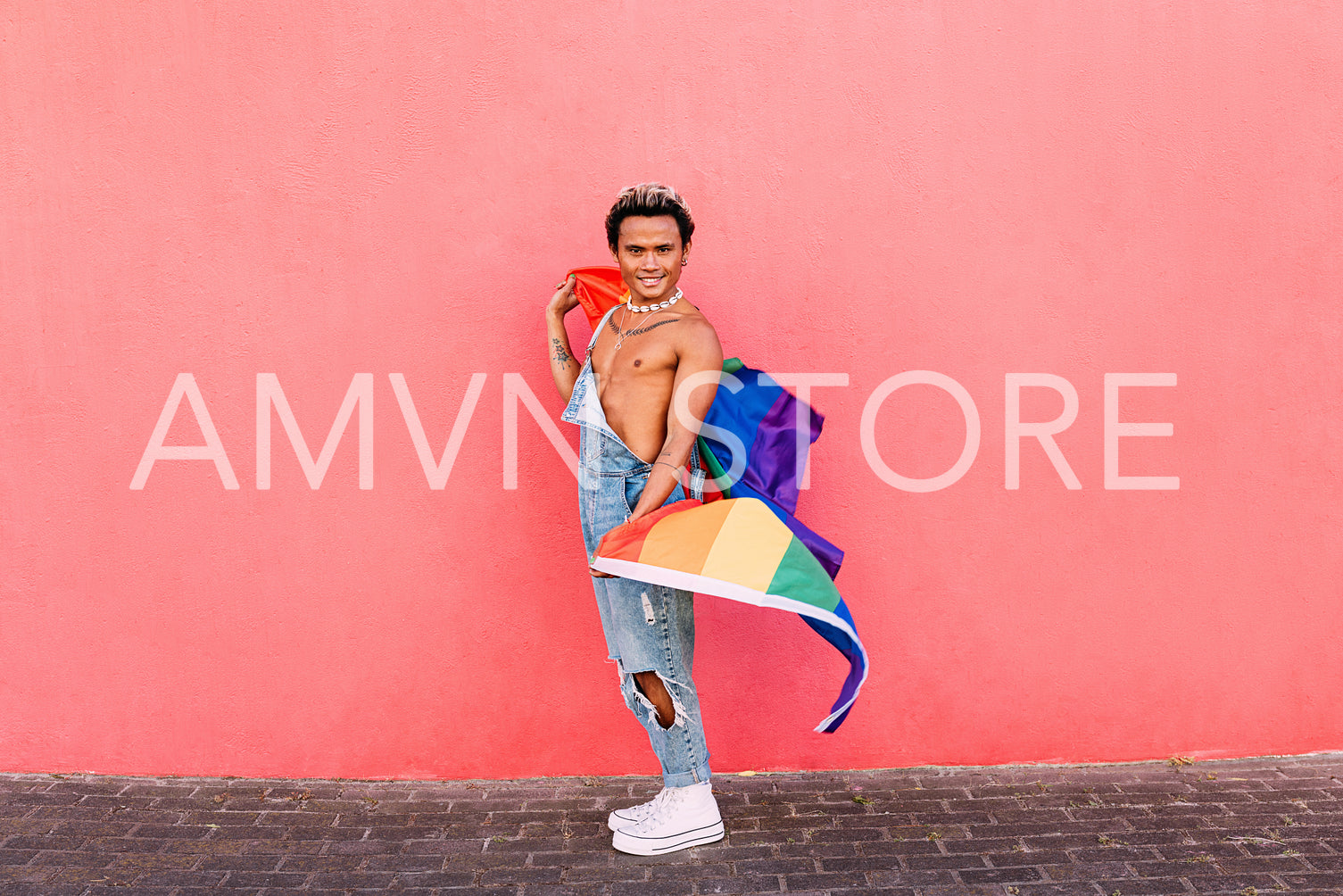 Young confident guy holding a rainbow LGBT flag and looking at camera at pink wall