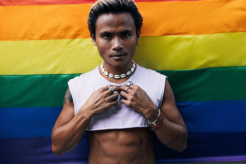 Portrait of a young stylish guy against LGBT rainbow flag looking at camera