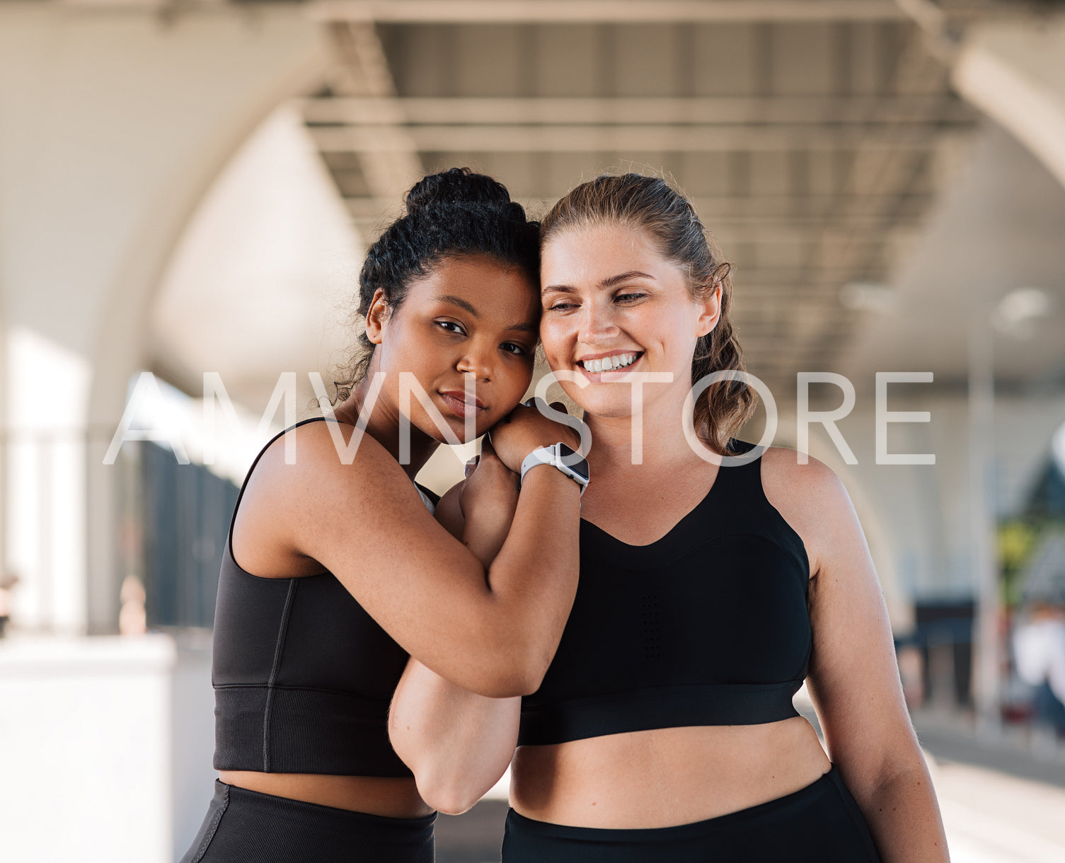 Two plus-size female friends in sportswear are standing together outdoors. Young women relaxing after intense workout hugging each other.