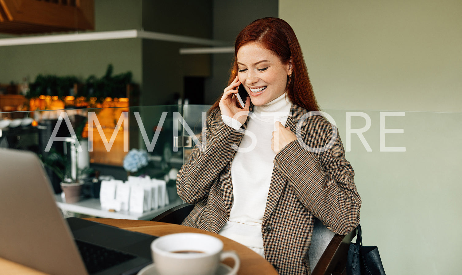 Smiling businesswoman with ginger hair talking on a smartphone. Cheerful female sitting at a table in a cafe and having a mobile phone conversation.