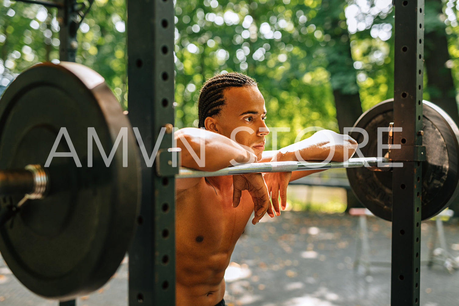 Side view of a bare-chest athlete standing outdoors leaning on a weight bar	