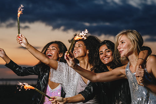 Happy friends with sparklers at sunset. Four laughing friends celebrating with fireworks outdoors.