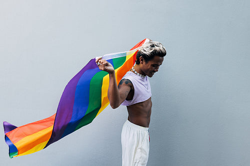 Side view of a young stylish man in stylish clothes walking with rainbow LGBT flag