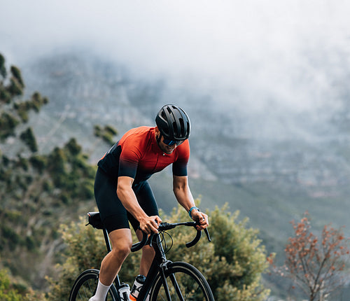 Cyclist on road bike riding in wild terrain. Athlete going up on hill on bicycle.