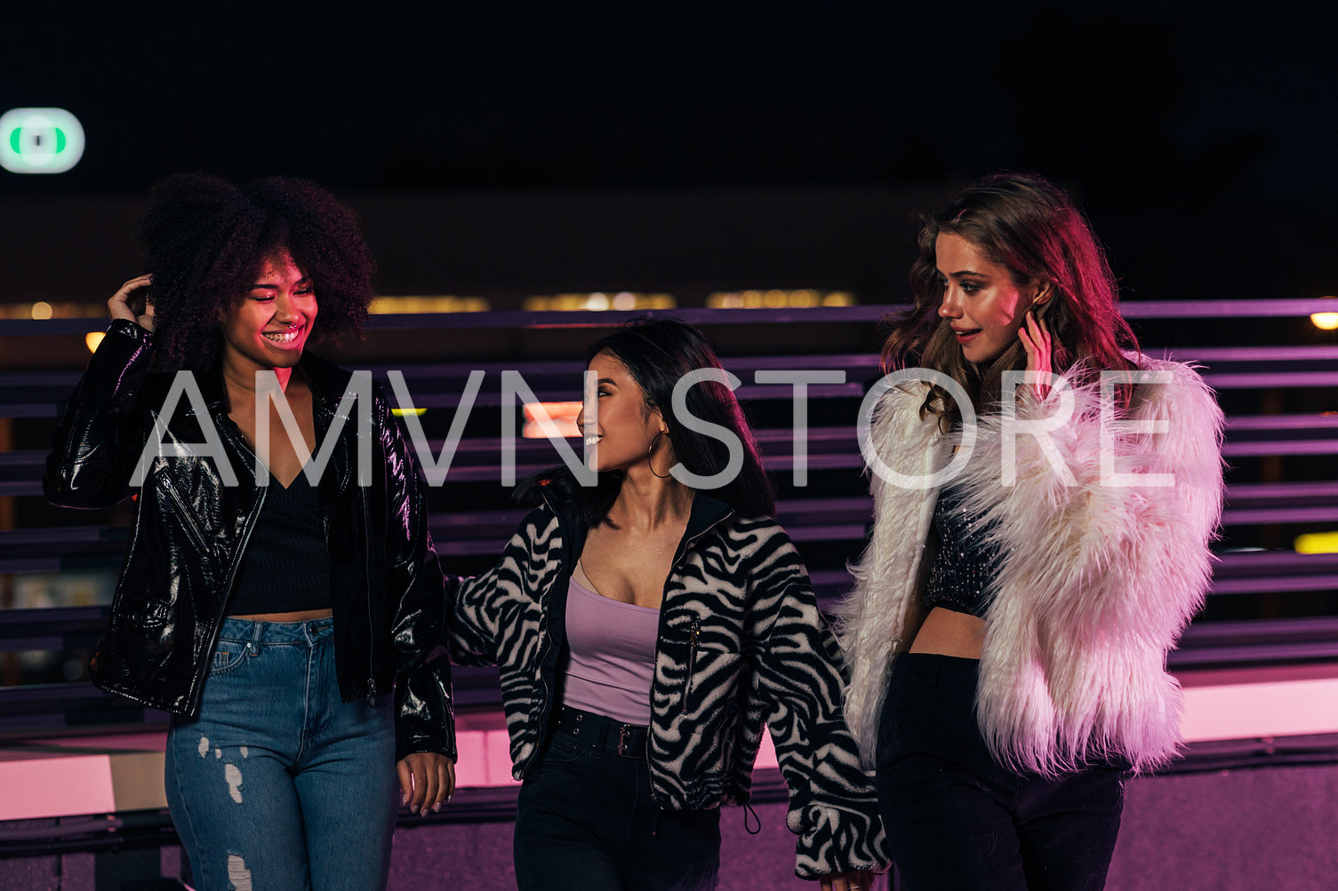 Three cheerful women walking on a roof under neon lights at night	