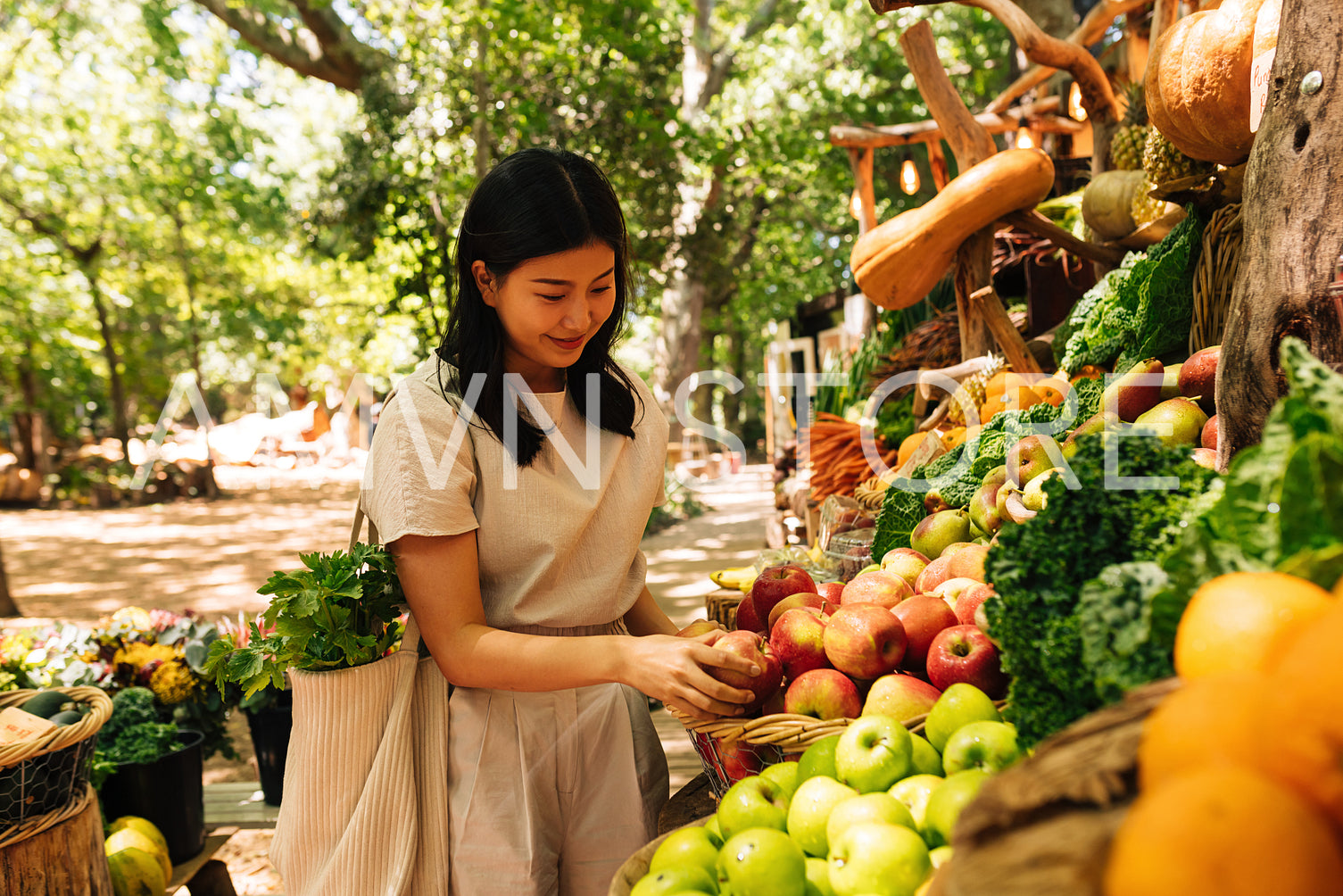 Smiling Asian woman choosing fruits. Female with a shopping bag at an outdoor market.