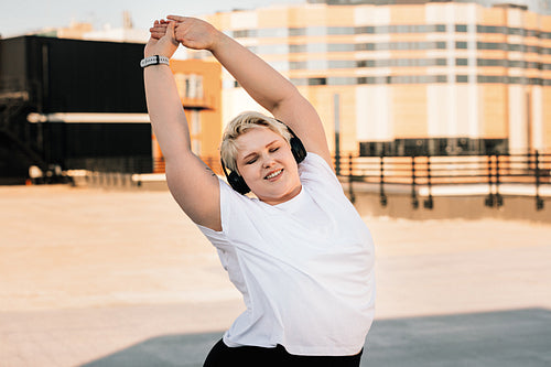 Happy woman with plus size body doing warming up exercises before workout