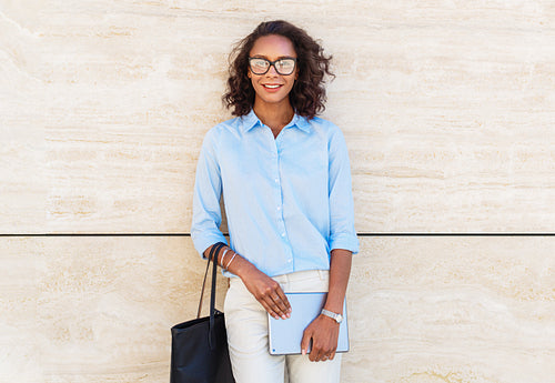 Smiling businesswoman wearing eyeglasses, standing at building with digital tablet in hands