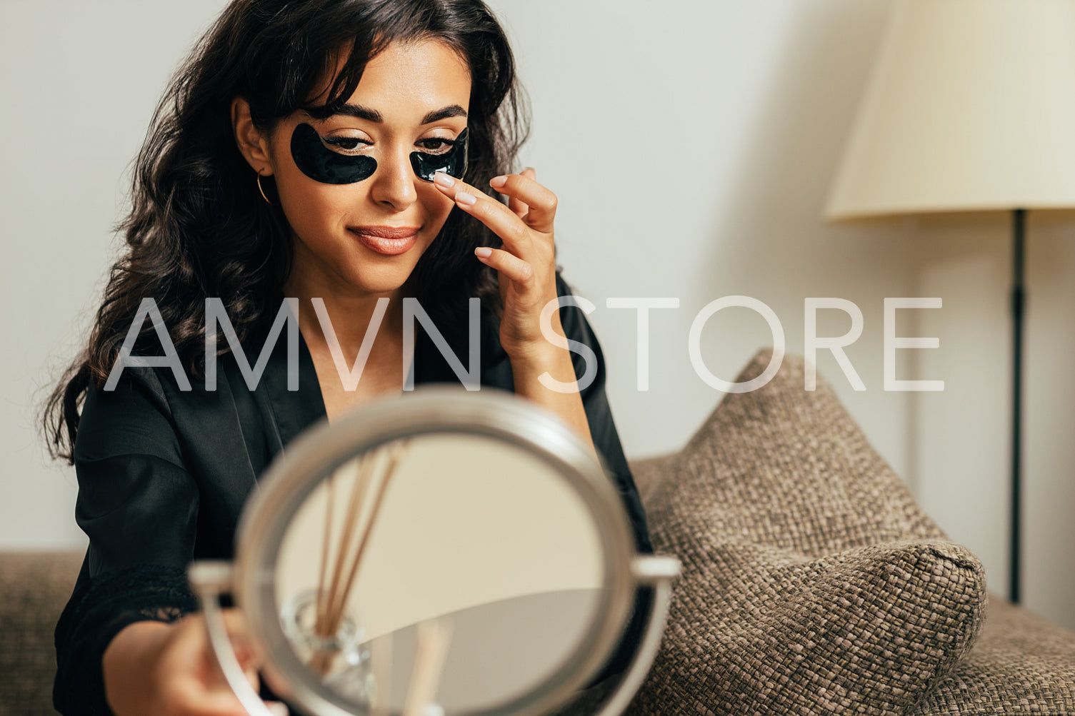 Middle east woman sitting in front of a mirror on a couch applying eye patch	