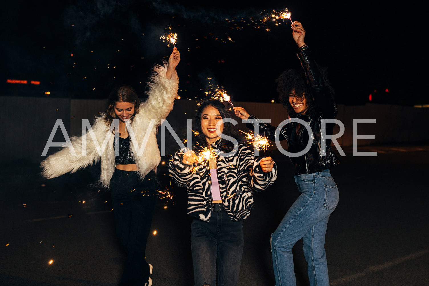 Three stylish girls having fun while walking with sparklers on city street at night	