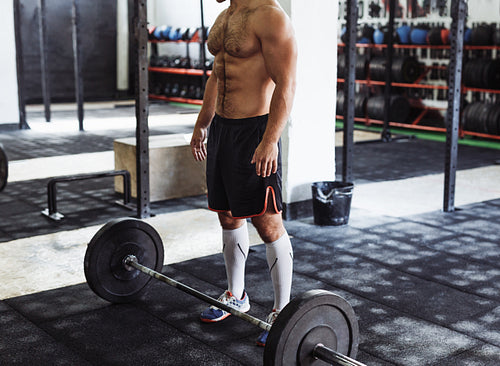 Unrecognizable man standing with heavy weights barbell on gym floor