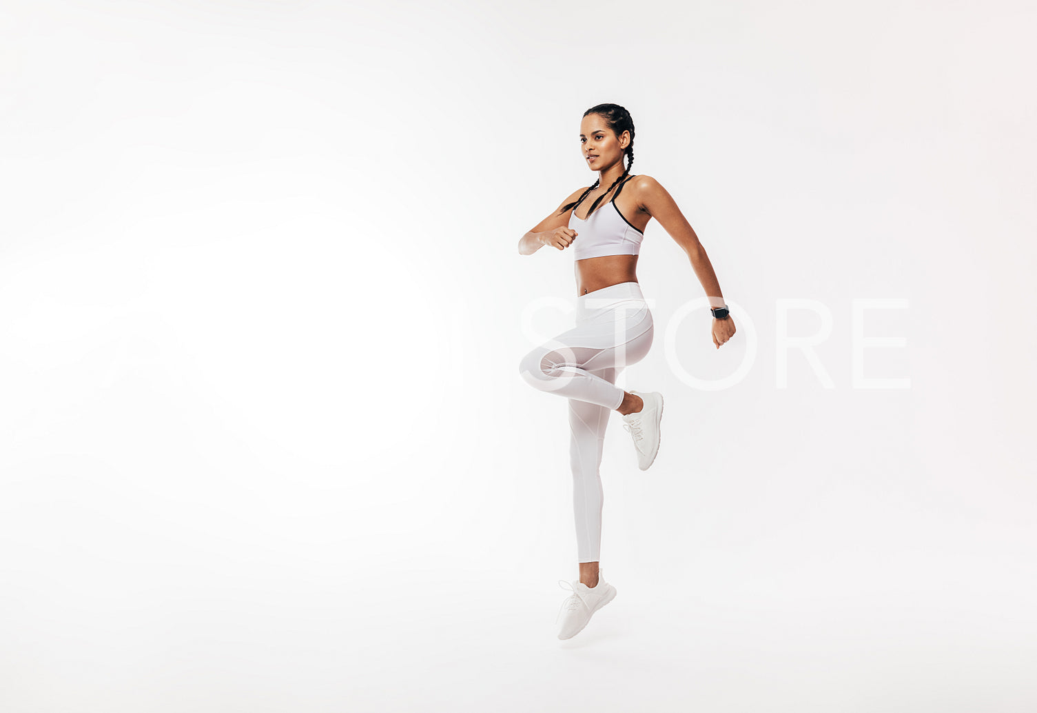 Young fit woman exercising over white background. Female in white sportswear jumping indoors.	