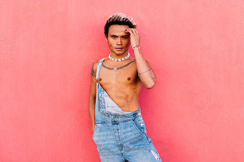 Handsome guy wearing denim overalls posing against pink background