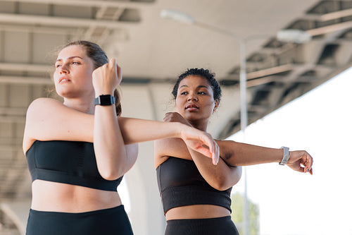 Two young female friends practicing together outdoors. Young women with plus-size bodies stretch their hands before workout.