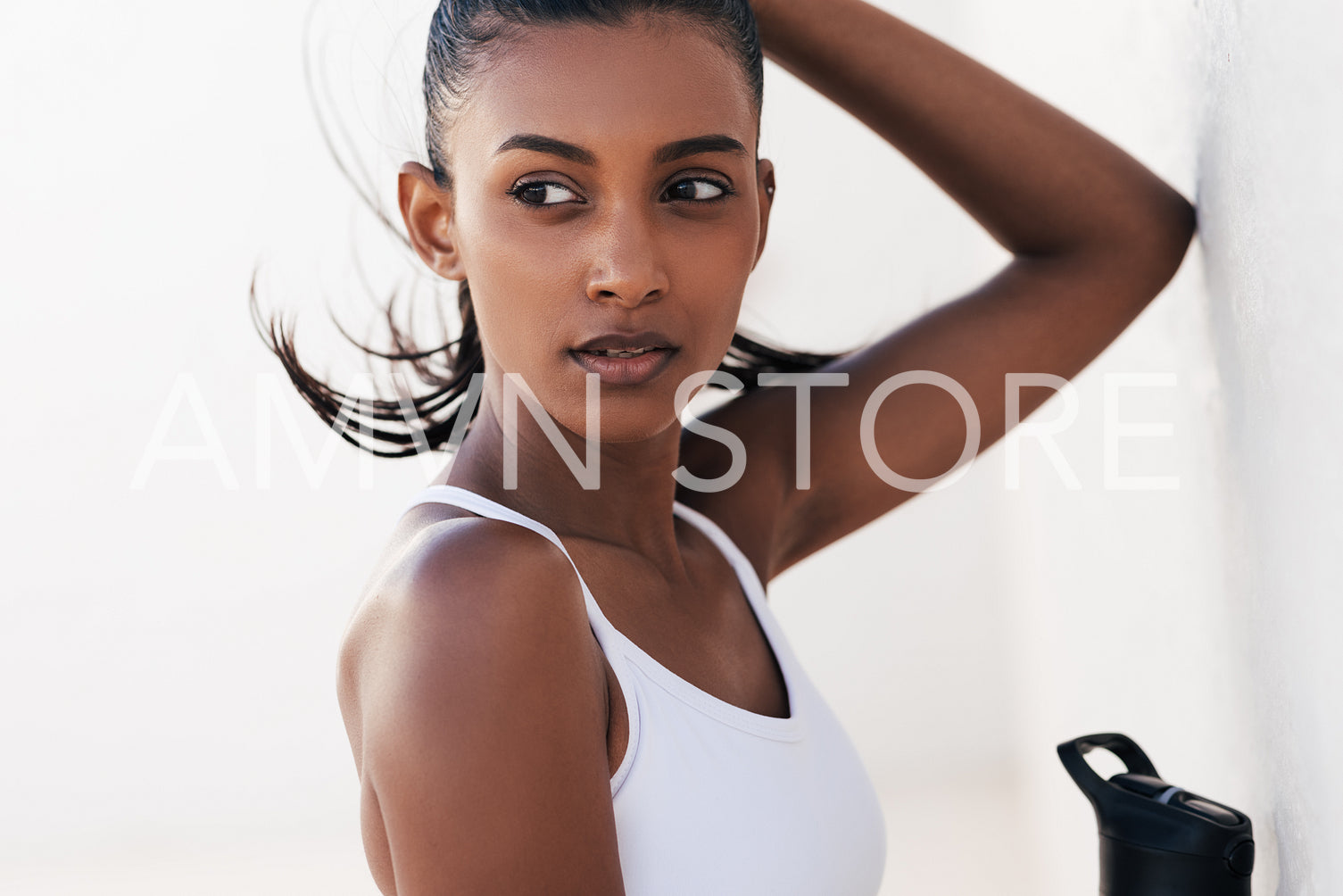 Portrait of a beautiful sportswoman relaxing at a white wall. Young female leaning wall looking away while taking a break.