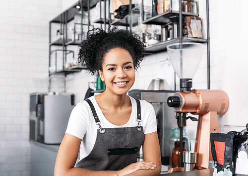 Portrait of a smiling barista with curly hair. Young female working as a barista in a coffee shop.