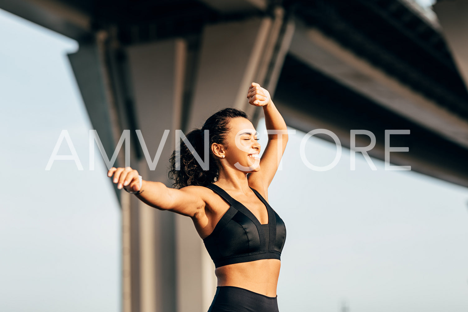 Happy woman in sportswear warming up before fitness training under a highway	